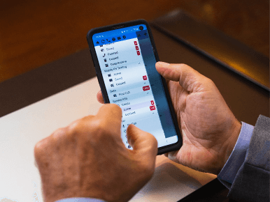 Closeup of a funeral director's hands holding a cell phone with the ASD mobile app menu open