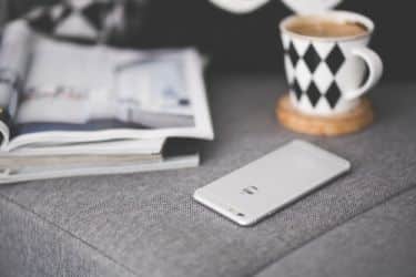 Phone, coffee cup, and stack of magazines sitting on a couch